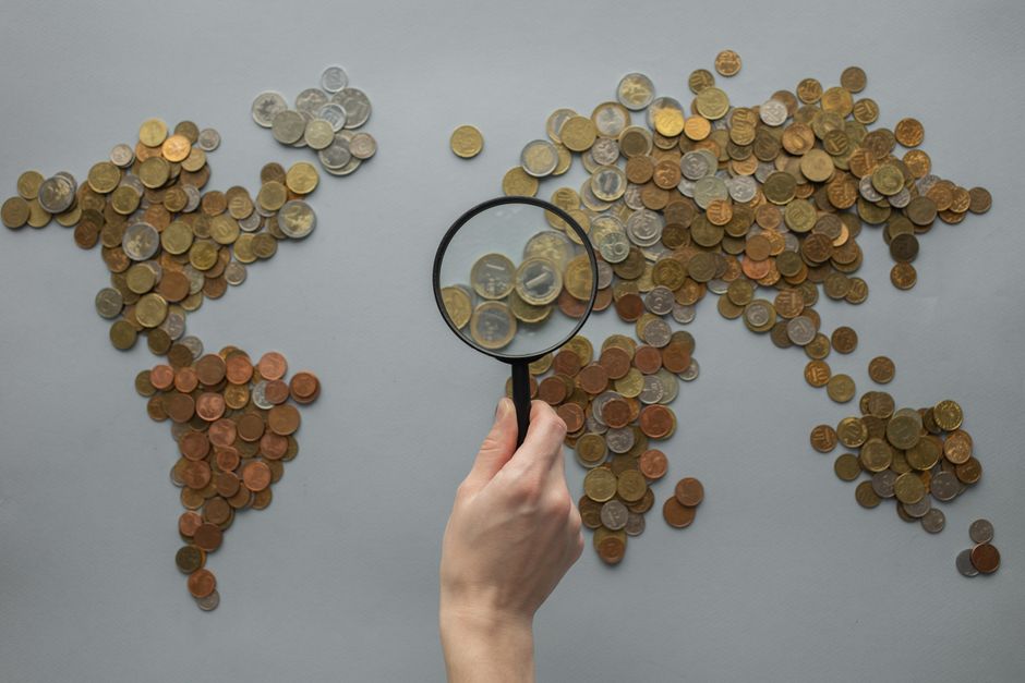 A hand holding a magnifying glass over a world map, suggesting curiosity and everyday discovery.