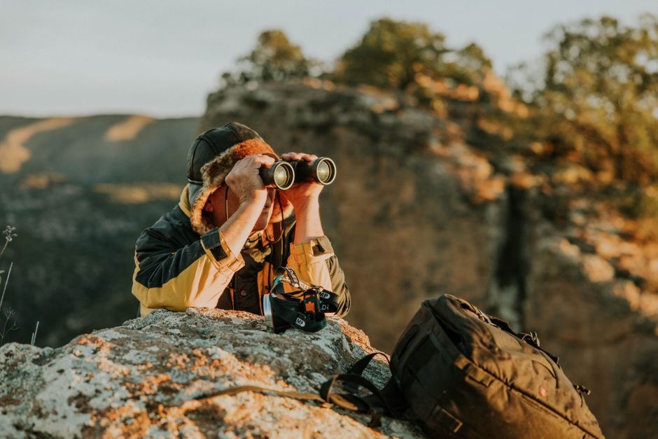 A photographer with a compact camera taking in a wide landscape from a rocky viewpoint.